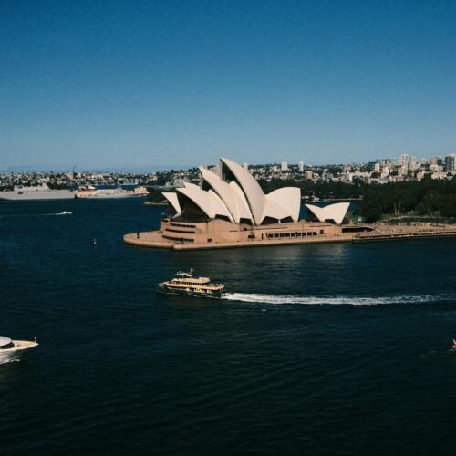 A breathtaking aerial view capturing the iconic Sydney Opera House surrounded by ferry boats on a sunny day.
